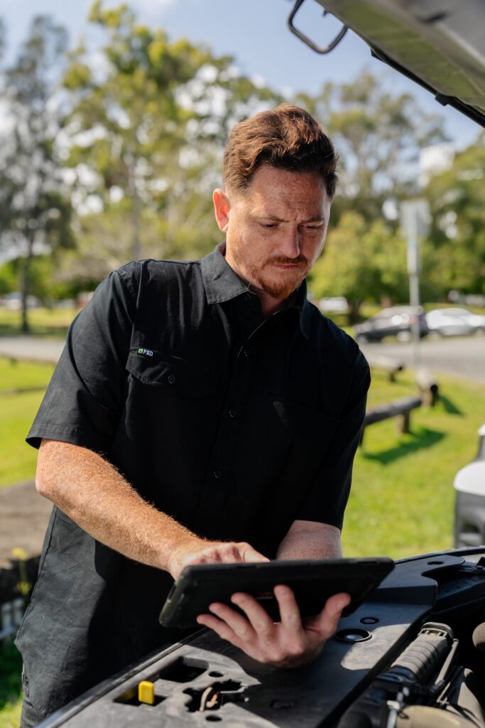 Inspector recording QLD safety certificate results on a tablet over the engine bay