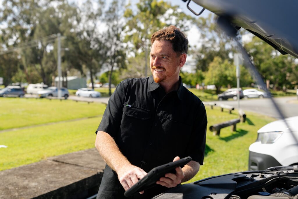 Smiling inspector with a tablet at the bonnet during a QLD safety certificate inspection